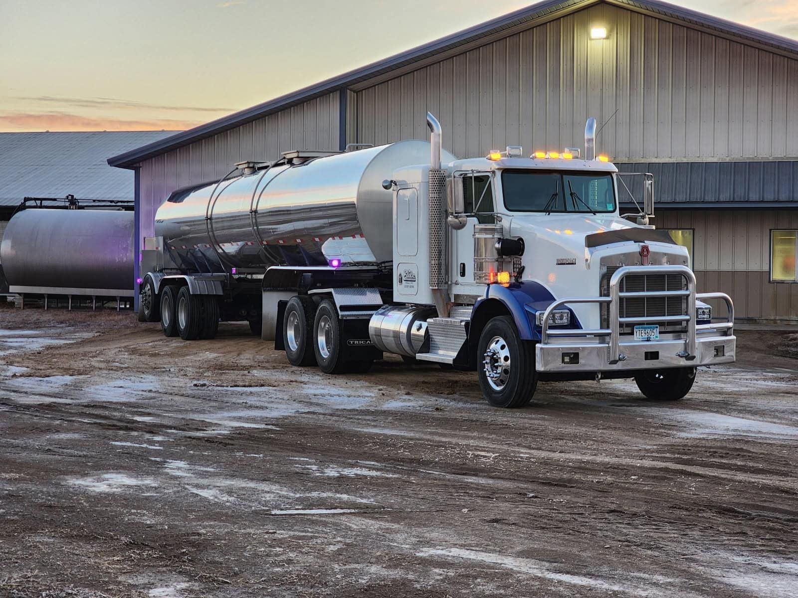 Elite Transport Group stainless steel milk tanker parked outside a dairy barn